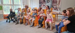 Dzieci siedzą na krzesełkach i słuchają koncertu muzycznego