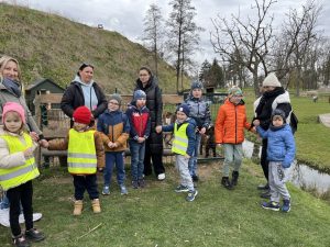 Dzieci z opienunami stoją przed zagrodą ze zwierzętami- kózki.