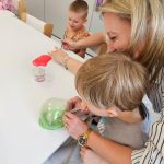 Dzieci bawią się kolorowymi slime- tworzą bańki dmuchając w nie słomką.