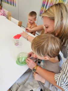 Dzieci bawią się kolorowymi slime- tworzą bańki dmuchając w nie słomką.