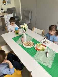 Dzieci siedzą przy stoliczku i jedzą świąteczne śniadanie.