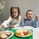 Dzieci siedzą przy stoliczku i jedzą świąteczne śniadanie.