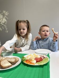 Dzieci siedzą przy stoliczku i jedzą świąteczne śniadanie.