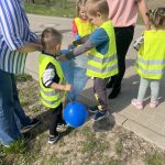 Dzieci sprzątają swoją okolicę. Wrzucają w rękawiczkach do worków znalezione śmieci.
