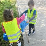 Dzieci sprzątają swoją okolicę. Wrzucają w rękawiczkach do worków znalezione śmieci.