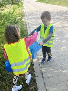 Dzieci sprzątają swoją okolicę. Wrzucają w rękawiczkach do worków znalezione śmieci.