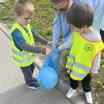 Dzieci sprzątają swoją okolicę. Wrzucają w rękawiczkach do worków znalezione śmieci.