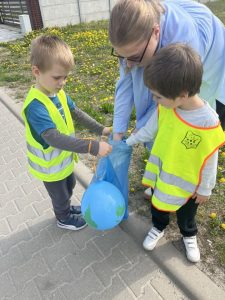 Dzieci sprzątają swoją okolicę. Wrzucają w rękawiczkach do worków znalezione śmieci.