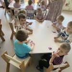 Dzieci siedzą przy stoliczkach i bawią się fioletowym slimem.