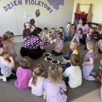 Nauczyciel podaje dzieciom z zawiązanymi oczami do spróbowania różnych fioletowych owoców i warzyw.