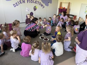Nauczyciel podaje dzieciom z zawiązanymi oczami do spróbowania różnych fioletowych owoców i warzyw.