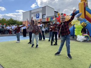 Siedmioro chłopców występujących przed publicznością, trzymających gitary. Chłopcy mają podniesioną jedną rękę do góry. W tle widać osoby dorosłe.