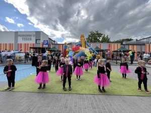 Grupa dzieci występująca przed publicznością. W tle widać zamek dmuchany oraz budynek przedszkola.