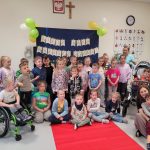 Grupa dzieci stoi na wybiegu z okazji Dnia Godności Osób z Niepełnosprawnościami.