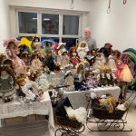 Kolekcja porcelanowych lalek ułożone na białych stołach. Obok stoi starszy mężczyzna.