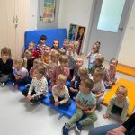 Grupa dzieci siedzi na niebieskim dywanie i ogląda lalki z porcelany.