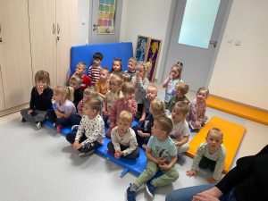 Grupa dzieci siedzi na niebieskim dywanie i ogląda lalki z porcelany.