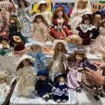 Kolekcja porcelanowych lalek ułożone na białych stołach.
