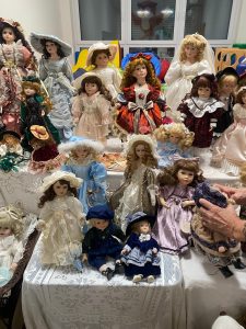 Kolekcja porcelanowych lalek ułożone na białych stołach.