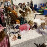 Kolekcja porcelanowych lalek ułożone na białych stołach.