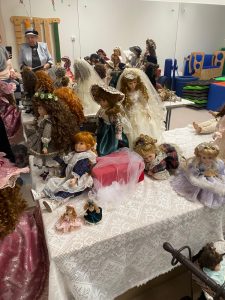 Kolekcja porcelanowych lalek ułożone na białych stołach.