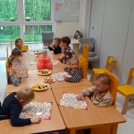 Dzieci siedzą przy stoliku i częstują się przekąskami urodzinowymi.