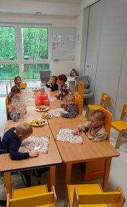 Dzieci siedzą przy stoliku i częstują się przekąskami urodzinowymi.