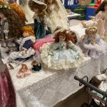 Kolekcja porcelanowych lalek ułożone na białych stołach.