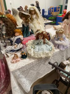Kolekcja porcelanowych lalek ułożone na białych stołach.