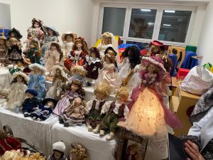 Kolekcja porcelanowych lalek ułożone na białych stołach.