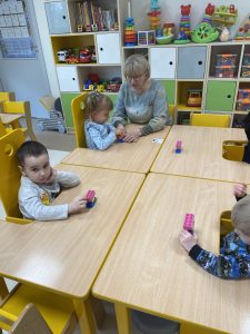 Dzieci z Panie przy stolikach W rękach trzymają ciastolinę i klocki