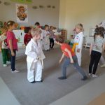Dwanaścioro dzieci i Pan stojący na dywanie. Czworo dzieci i mężczyzna są ubrani w strój do Taekwondo.