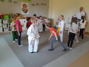 Dwanaścioro dzieci i Pan stojący na dywanie. Czworo dzieci i mężczyzna są ubrani w strój do Taekwondo.
