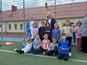 Dziesięcioro dzieci i dwie Panie znajdujący się na boisku sportowym. Dzieci maja założone medale.