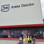 Sześcioro dzieci i cztery Panie pozujące do zdjęcia przed budynkiem 3mk Arena Ostrów. Dwoje dzieci siedzi w wózkach.