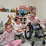 Dwójka dzieci siedzi na podłodze , jeden chłopiec na wózku inwalidzkim
