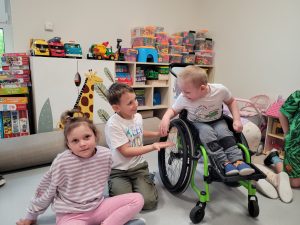 Dwójka dzieci siedzi na podłodze , jeden chłopiec na wózku inwalidzkim