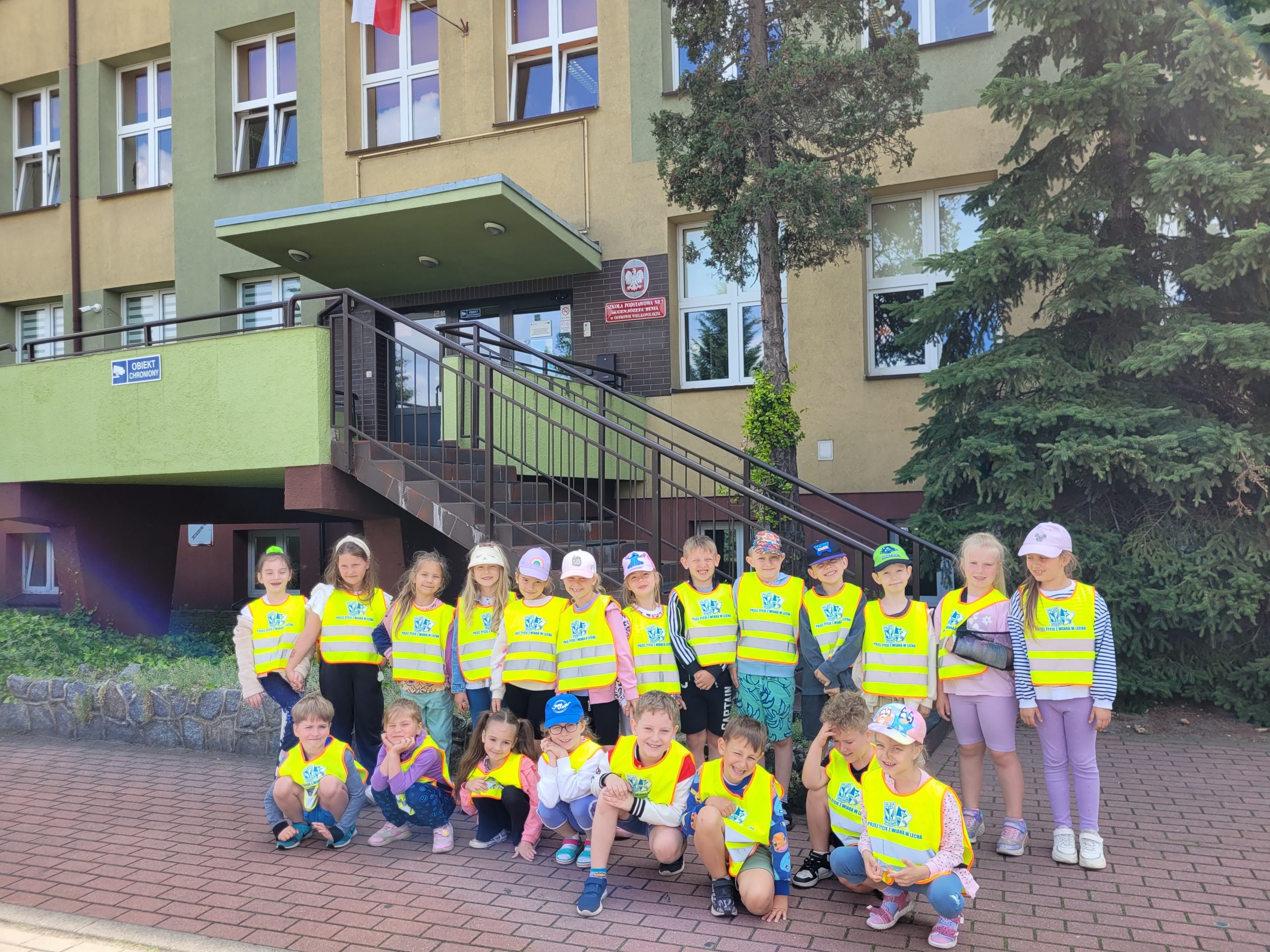 Dzieci stoją przed budynkiem szkoły i pozują do zdjęcia