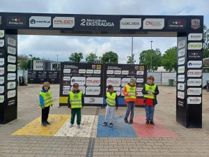 Pięcioro chłopców ubranych w kamizelki odblaskowe, stojących na stadionie żużlowym.