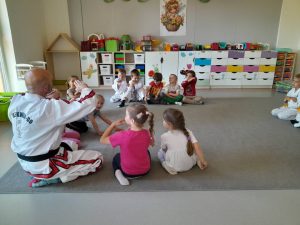 Grupa dzieci z instruktorem w białym kimono demonstrują pokazane chwyty