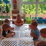 Grupa dzieci siedzi przy stoliczkach i ozdabia lizaki