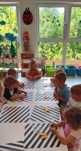 Grupa dzieci siedzi przy stoliczkach i ozdabia lizaki