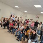 Duża grupa rodziców siedzi na białych krzesłach i ogląda tańczące dzieci.