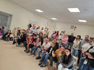 Duża grupa rodziców siedzi na białych krzesłach i ogląda tańczące dzieci.