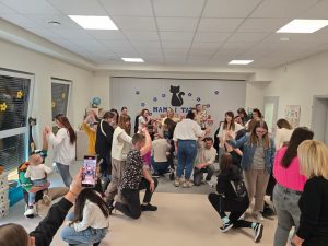 Duża grupa rodziców tańczy w parach na szarym dywanie.