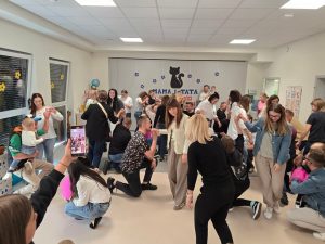 Duża grupa rodziców tańczy w parach na szarym dywanie.