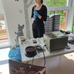 Pani prowadząca czekoladowe warsztaty stoi i przemawia do dzieci, opowiada im co będą robić, historię czekolady itp. Przed nią znajdują się sprzęty do tworzenia czekolady.