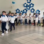 Grupa dzieci kończących przedszkole występuje na uroczystości dla swoich rodziców i zaproszonych gości. Dzieci są odświętnie ubrane, dziewczynki mają długie, tiulowe spódniczki, na głowach białe opaski z niebieskim kwiatem i modrakowe bluzeczki z krótkim rękawem. Chłopcy mają modrakowe muchy przy kołnierzykach swoich białych koszul, ciemne długie spodnie. Wszystkie dzieci wyglądają elegancko. Tańczą parami, tańczą poloneza. Tak więc para za parą. W tle dekoracje.