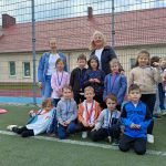 Grupa dzieci wraz ze swoją panią pozują do zdjęcia w strojach sportowych i medalach na szyjach.