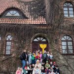 Grupa 20 dzieci w wieku przedszkolnym wraz z 2 paniami pozuje do zdjęcia na schodach zamku w Gutowie.
